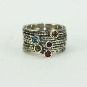 Op de afbeelding: Een zilveren ring met zes gekleurde edelstenen gezet in een gehammerde band. De ring bestaat uit vijf gestapelde banden.