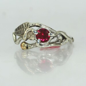 May include: A silver ring with a red gemstone set in a twisted band, accented with a leaf design.