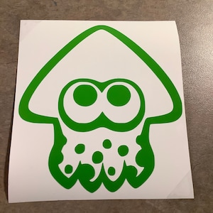 May include: Green vinyl sticker of a cartoon squid with a white hat and large eyes. The squid has a spotted body.