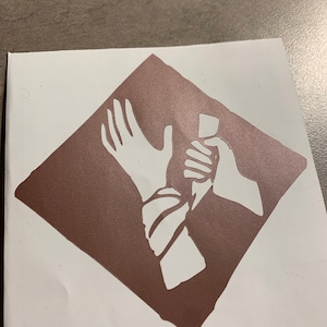 May include: A white silhouette of two hands, one holding a knife, the other with a wrist bound, against a brown diamond-shaped background.
