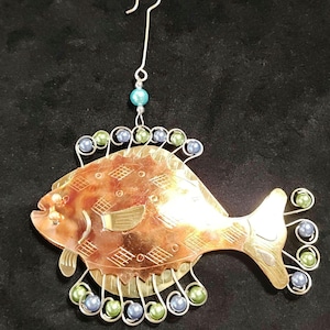 May include: A decorative fish ornament with a copper-colored body and etched details. The fish has silver wire accents and is adorned with blue and green beads. A silver hook is attached for hanging.