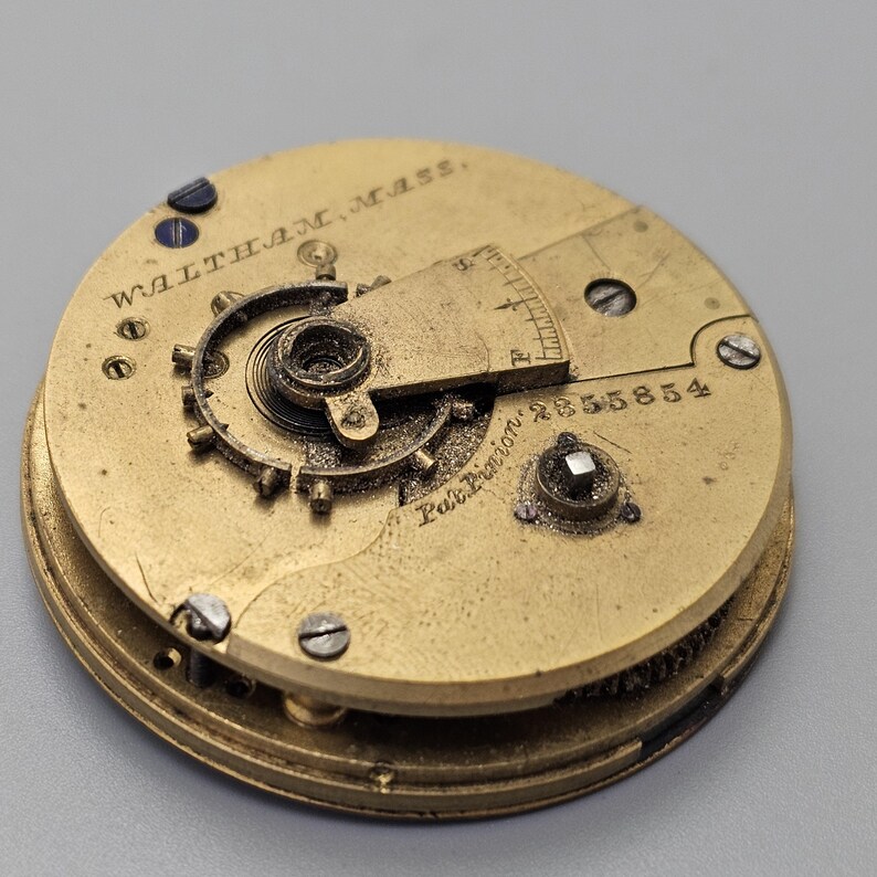 Puede incluir: Primer plano de un movimiento de reloj de bolsillo dorado con la inscripci&oacute;n "Waltham, Mass." y "Pat. Pending" junto con el n&uacute;mero de serie "558554".