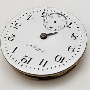 May include: Close-up of an antique Elgin pocket watch face. The white face features black numerals, a smaller seconds dial, and a black hand. The word "Elgin" is printed on the face.