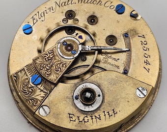 Op de afbeelding: Close-up van het uurwerk van een Elgin Nat'l. Watch Co. zakhorloge. Het goudkleurige mechanisme heeft ingewikkelde details, waaronder gegraveerde patronen, blauwe schroeven en de tekst "Elgin Nat'l. Watch Co." en "Elgin Ill.". Het serienummer "125547" is ook zichtbaar.