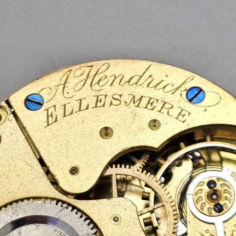 May include: Close-up of a gold-toned pocket watch movement with the inscription "A Hendrick Ellesmere".