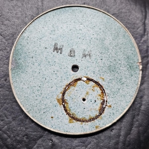 Puede incluir: Una esfera de reloj redonda de color azul claro con un anillo marr&oacute;n alrededor del agujero central. La esfera del reloj tiene el texto "M & M" escrito en ella.