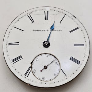 May include: Antique pocket watch face with a white background, black Roman numerals, and a smaller seconds dial. The watch hands are blue, and the text "ELGIN NAT'L WATCH CO" is visible.