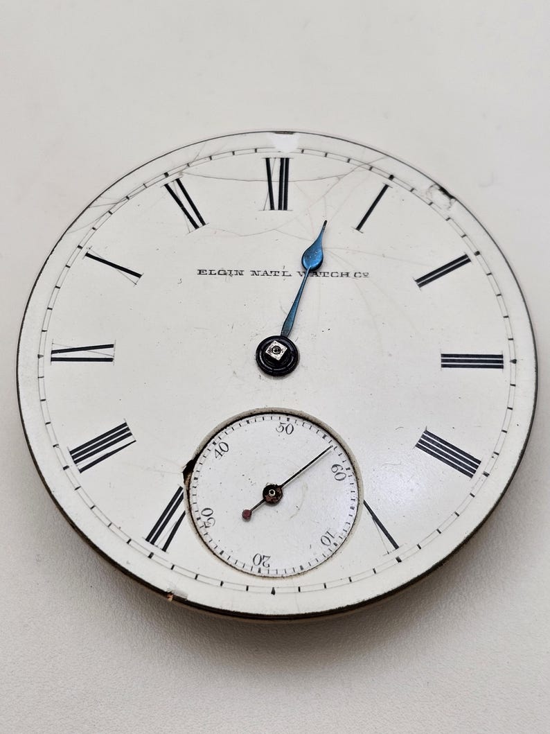May include: Antique pocket watch face with a white background, black Roman numerals, and a smaller seconds dial. The watch hands are blue, and the text "ELGIN NAT'L WATCH CO" is visible.