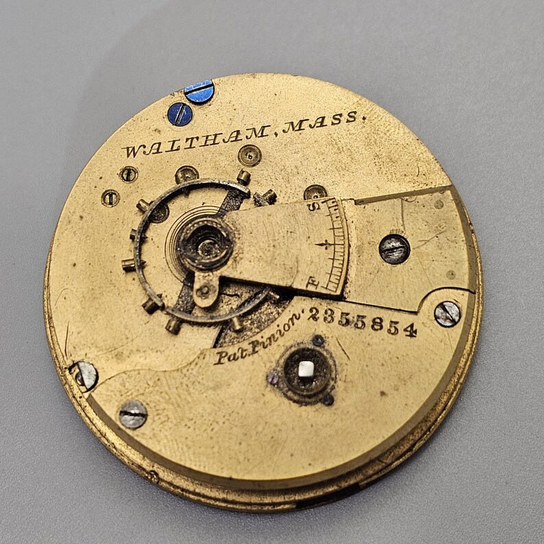 Puede incluir: Primer plano de un movimiento de reloj de color dorado con el texto "WALTHAM, MASS." y "Pat. Pinion 2355854".