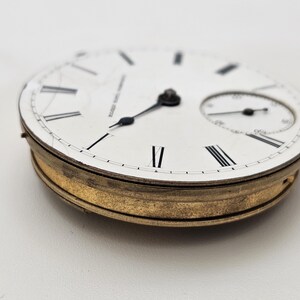 May include: A vintage pocket watch face with a white dial, black Roman numerals, and a smaller subdial. The watch has black hands and a gold-toned bezel. The text "WALTHAM U.S.A. CO." is visible on the dial.