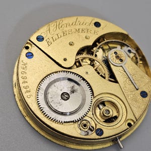 May include: Close-up of a gold-colored pocket watch movement with the inscription "A Hendrick Ellesmere" and the number "694945".