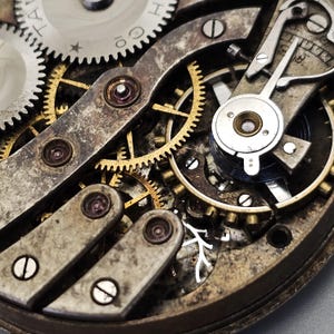 May include: Close-up of a vintage watch mechanism. The image showcases intricate gears, levers, and screws in shades of silver, gold, and bronze. The aged components reveal the watch's internal workings, highlighting its mechanical complexity and craftsmanship.
