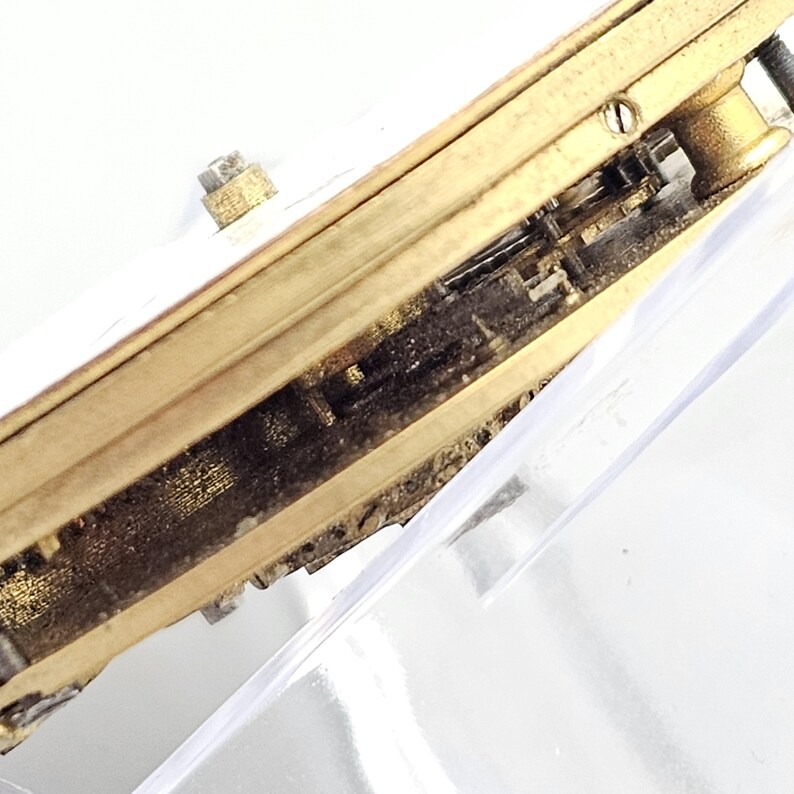 Puede incluir: Primer plano de la parte inferior de un reloj dorado con un mecanismo de engranaje visible.