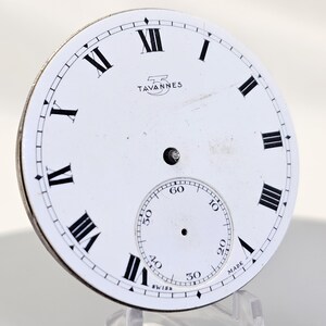 May include: A white watch face with black Roman numerals and a smaller seconds dial. The brand name "TAVANNES" is printed above the center. The word "SWISS" is printed at the bottom.