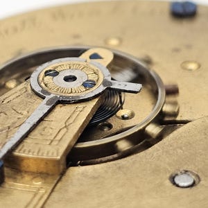 May include: Close-up of a vintage watch mechanism. The image showcases intricate details of the watch's internal components, including gears, springs, and a balance wheel. The metal parts have a gold and silver finish, with blue accents. The watch face is visible.