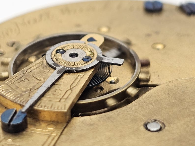 May include: Close-up of a vintage watch mechanism. The image showcases intricate details of the watch's internal components, including gears, springs, and a balance wheel. The metal parts have a gold and silver finish, with blue accents. The watch face is visible.