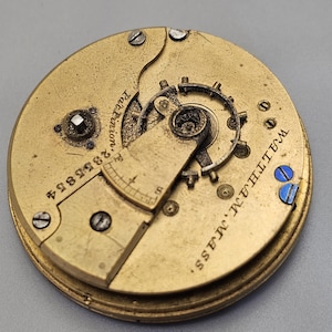 Puede incluir: Primer plano de un movimiento de reloj de bolsillo de color dorado con la inscripci&oacute;n "Waltham, Mass. E.T.C. Co. Patent, 18884" visible en la parte posterior.
