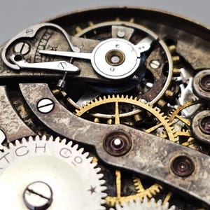May include: Close-up of a vintage watch mechanism. The image showcases intricate gears, springs, and levers in shades of gold, silver, and bronze. The watch components are arranged in a complex, detailed pattern, highlighting the craftsmanship of the timepiece.