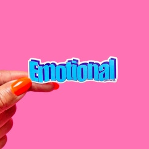 May include: A blue and purple sticker with the word "Emotional" in a bold, 3D-style font. The sticker is held in a hand against a pink background.