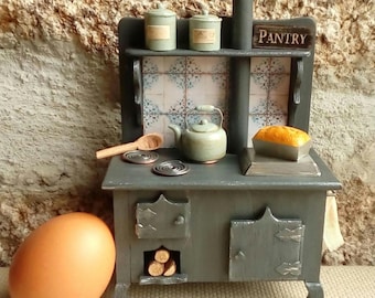 May include: A miniature gray stove with a small kettle, wooden spoon, and two canisters. A loaf of bread sits on the stove top. The word "PANTRY" is on a sign above. An egg is in the foreground.