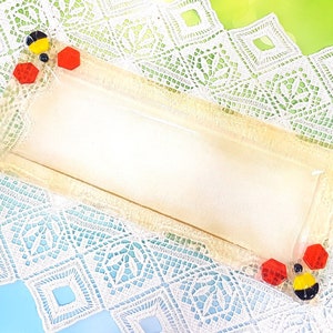 Może przedstawiać: Prostokątna szklana taca do serwowania w jasnobeżowym kolorze z podwyższonym rantem. Taca ma wzór pszczoły z czarnymi, żółtymi i czerwonymi akcentami.