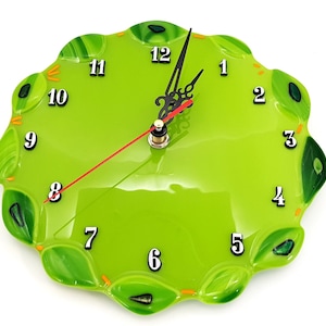 May include: A green glass clock with black numbers and hands. The clock face has a wavy, organic design with green and orange accents.