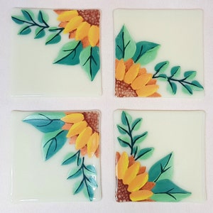 Può includere: Set di quattro sottobicchieri quadrati in ceramica con un design dipinto di girasoli e foglie verdi nell'angolo di ogni sottobicchiere.
