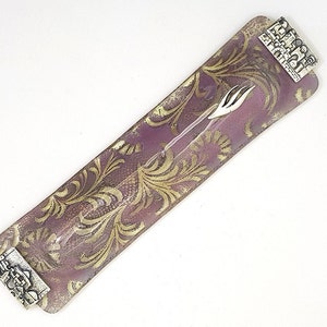 May include: A purple glass  Torah pointer holder with gold leaf accents and silver metal embellishments. The holder has a decorative floral pattern.