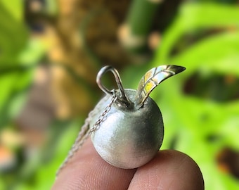 May include: A silver apple pendant with a gold leaf detail. The pendant is attached to a silver chain.
