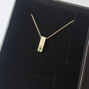 May include: A gold necklace with a small green gemstone set in a rectangular pendant. The necklace is displayed in a black velvet box.