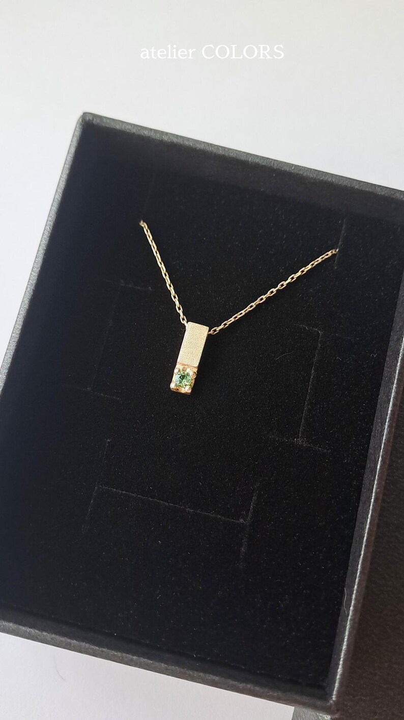 May include: A gold necklace with a small green gemstone set in a rectangular pendant. The necklace is displayed in a black velvet box.