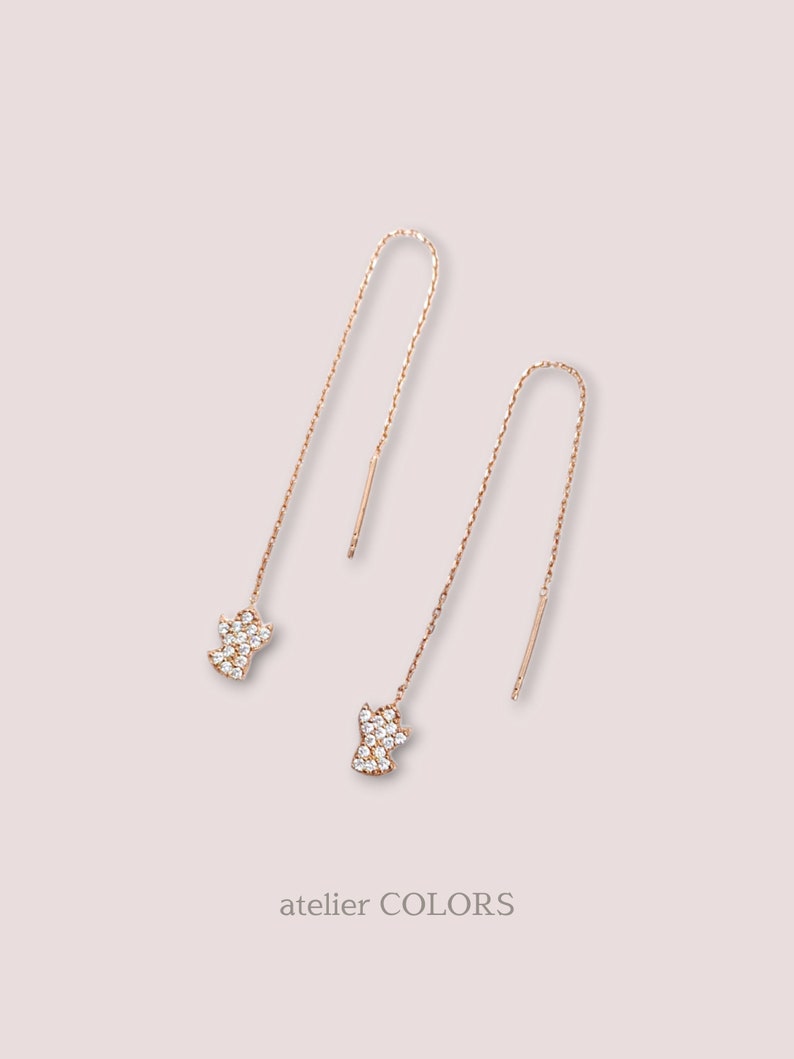 Puede incluir: Un par de pendientes colgantes de oro rosa con un peque&ntilde;o dije en forma de diamante en la parte inferior de cada pendiente. Los dijes est&aacute;n cubiertos de peque&ntilde;os diamantes de imitaci&oacute;n transparentes.