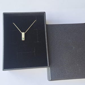 May include: A silver necklace with a small green gemstone pendant in a black velvet box.