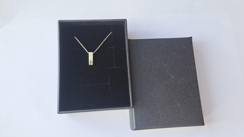 May include: A silver necklace with a small green gemstone pendant in a black velvet box.