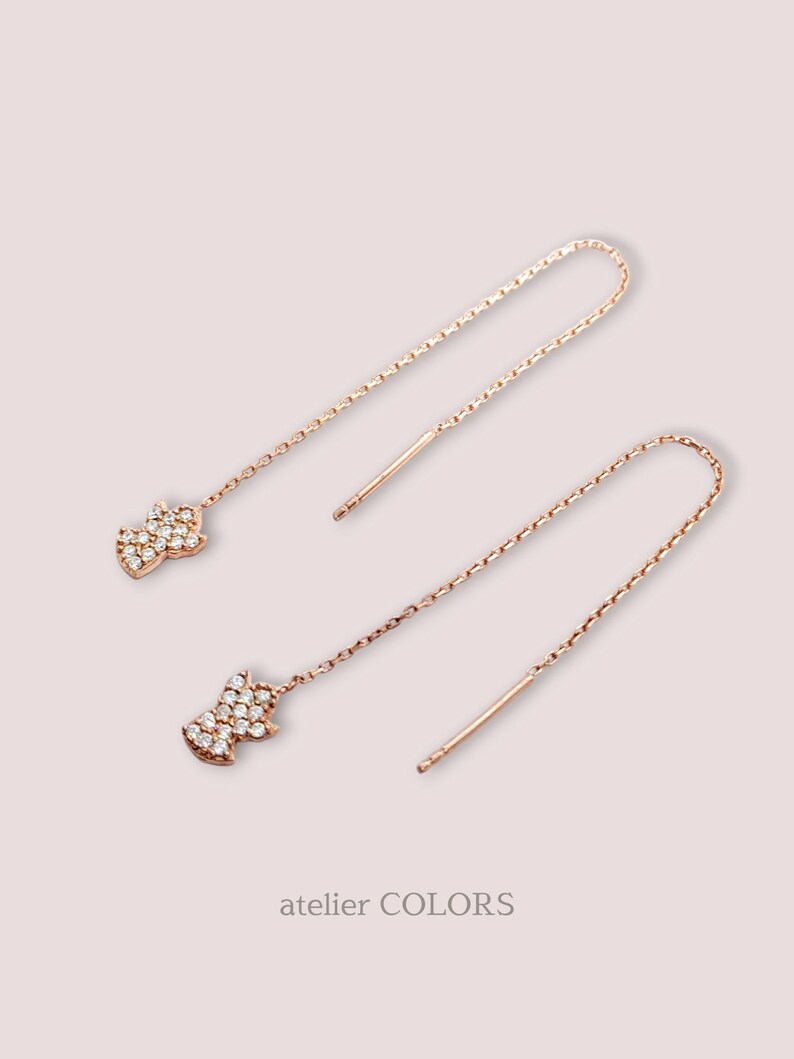 Puede incluir: Un par de pendientes de oro rosa con una cadena delicada y un peque&ntilde;o colgante en forma de diamante brillante.