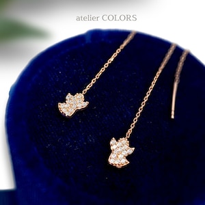 Puede incluir: Un par de delicados pendientes de oro con un dise&ntilde;o de &aacute;ngel colgante. Cada &aacute;ngel est&aacute; adornado con piedras transparentes brillantes.