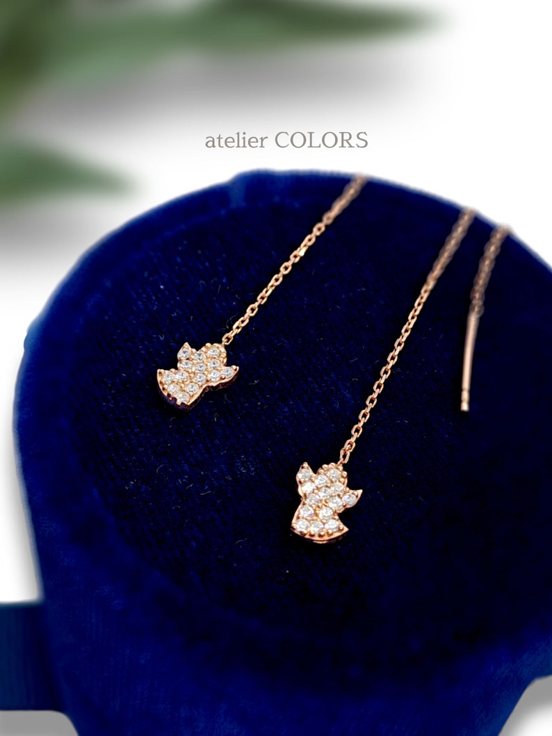 Puede incluir: Un par de delicados pendientes de oro con un dise&ntilde;o de &aacute;ngel colgante. Cada &aacute;ngel est&aacute; adornado con piedras transparentes brillantes.