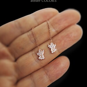 Puede incluir: Un par de pendientes colgantes de oro rosa con un dise&ntilde;o de huella de pata. Cada huella de pata est&aacute; adornada con piedras de circonita c&uacute;bica transparentes.