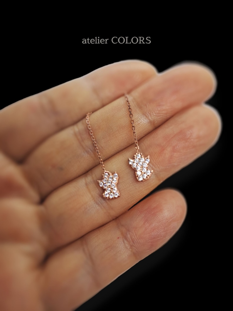 Puede incluir: Un par de pendientes colgantes de oro rosa con un dise&ntilde;o de huella de pata. Cada huella de pata est&aacute; adornada con piedras de circonita c&uacute;bica transparentes.