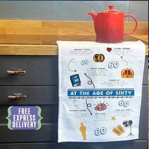 May include: A white tea towel with a blue and white illustration of a book and the text "At the age of sixty". The illustration is surrounded by a circle with the number 60 in it. The tea towel also features illustrations of a red heart, a crown, a brain, an Oscar statue, and a movie clapperboard. The text "Free Express Delivery" is in a green box on the left side of the tea towel.