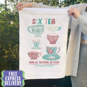 May include: White tea towel featuring six colourful teacups and saucers. The text reads "Six Tea and as tasteful as ever. Happy Birthday Moira."