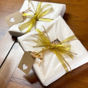 May include: Two gifts wrapped in white tissue paper with gold ribbon and brown paper tags. One tag has a heart cut out and the other has the word "Hello" written on it.