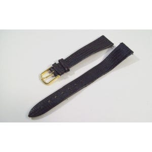 May include: A two-piece black watch strap with a textured surface and a gold-toned metal buckle. The strap features a series of adjustment holes on one side and a sliding keeper loop on the other, designed for securing a timepiece to the wrist.