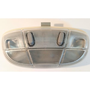 May include: An oval-shaped automotive overhead interior dome light assembly with a translucent ribbed plastic lens, featuring two gray rectangular push-button switches and integrated clear textured light panels.