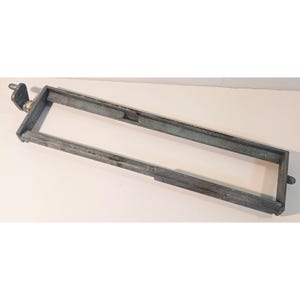 May include: A rectangular, weathered gray metal frame featuring a hinged attachment on one end and a small protruding tab on the opposite side. The structure is constructed from hollow, channel-shaped metal bars with visible signs of oxidation.