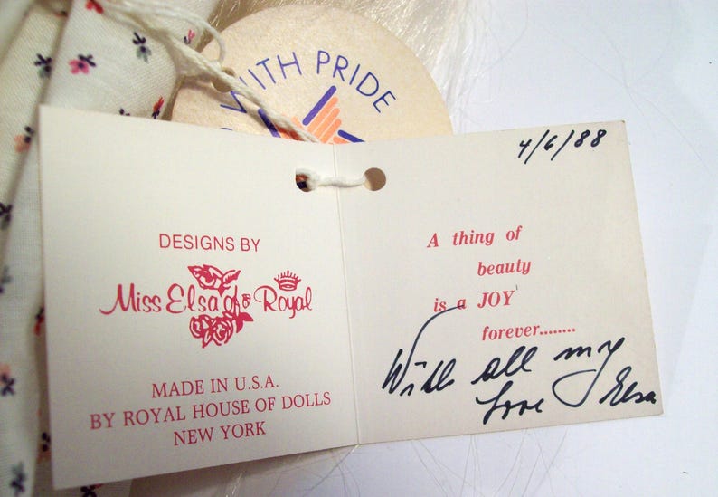May include: A white tag with pink lettering that reads "Designs by Miss Elsa of Royal" and "Made in U.S.A. by Royal House of Dolls New York". A second white tag with black lettering reads "A thing of beauty is a JOY forever... Will all my love Elsa". The date "4/6/88" is written in black ink on the top right corner of the second tag.