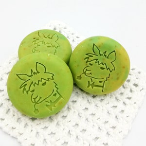 以下が含まれることがあります： ラマのデザインが施された緑色の石鹸が3つ。石鹸は白いレースの敷物の上に置かれています。