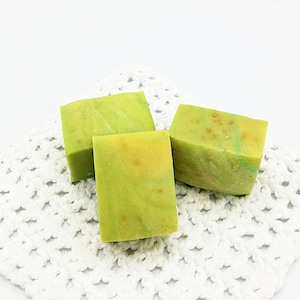 以下が含まれることがあります： 白いレースのドイリーの上に、緑と黄色の石鹸が3つ置かれています