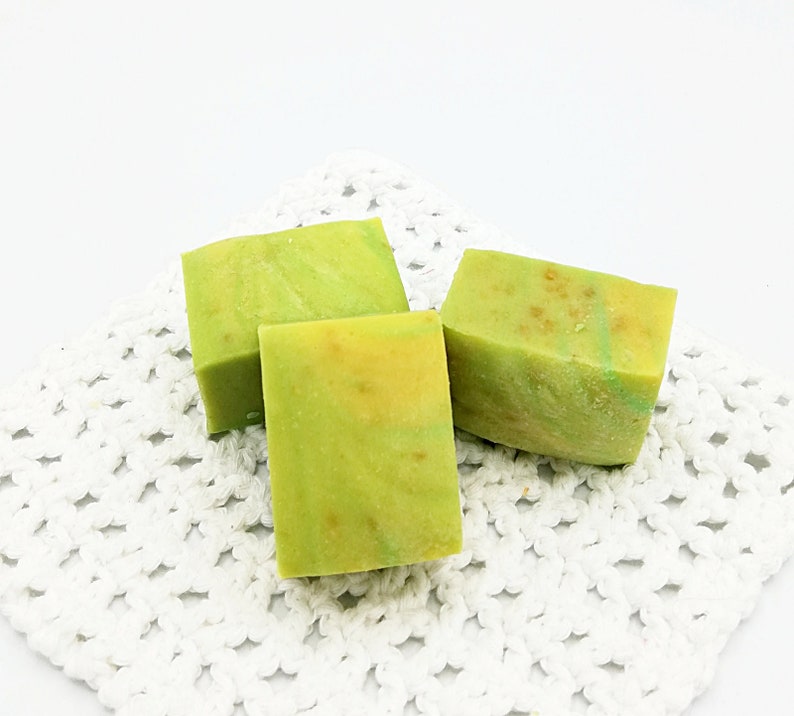 以下が含まれることがあります： 白いレースのドイリーの上に、緑と黄色の石鹸が3つ置かれています