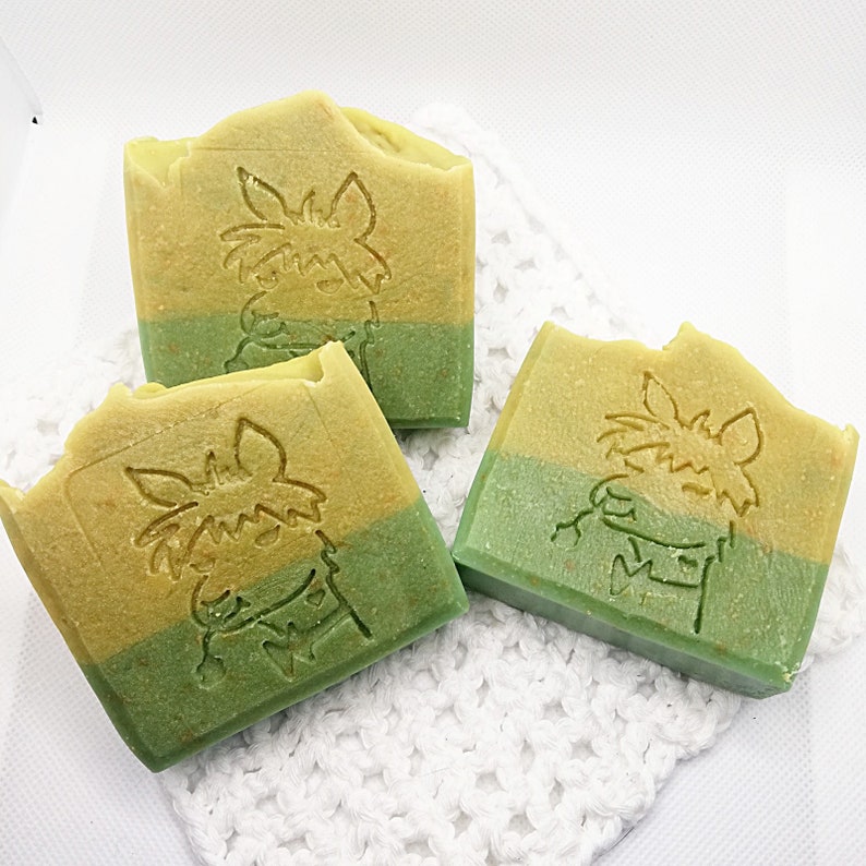以下が含まれることがあります： 緑と黄色のカラーリングで手作りされた石鹸が3つあります。各石鹸には、緑と黄色のデザインの漫画の動物が描かれています。